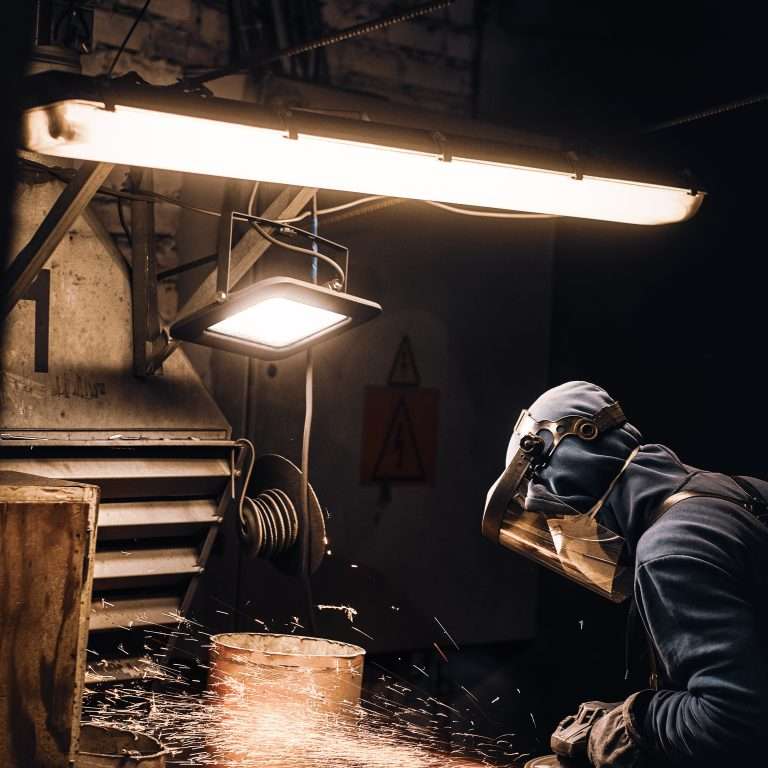 Man in protective mask is cutting metal and sparks are flying away.